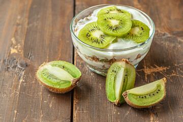 homemade delicious layered dessert of yogurt, muesli and kiwi fruit on a wooden table