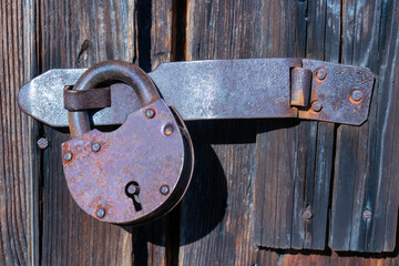 An old closed rusty barn lock hanging on the bracket of a wooden door. Front view. Close-up. Hard...