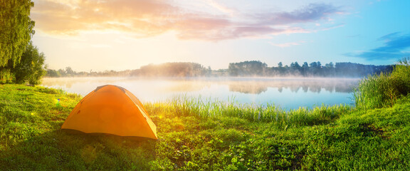 Orange tourist tent in green grass of lake shore