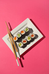 Plate with tasty maki rolls and wooden chopsticks on color background