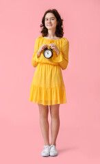Pretty teenage girl with alarm clock on pink background