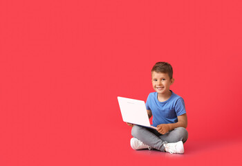 Cute little boy using laptop on red background