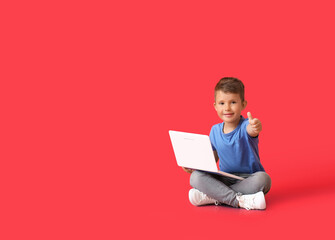 Cute little boy with laptop showing thumb-up on red background