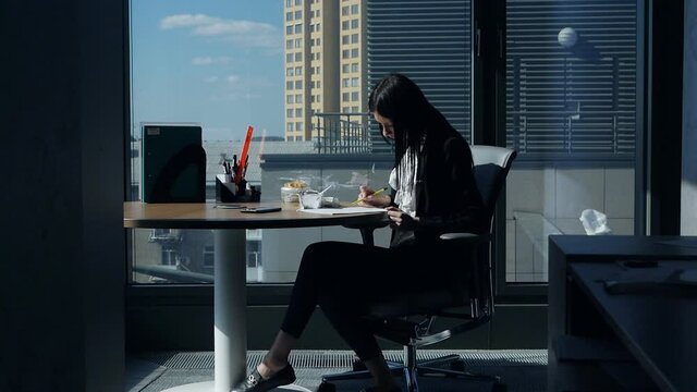 Businesswoman eating at workplace.Young woman in a modern beautiful office near the panoramic window dines and examines documents