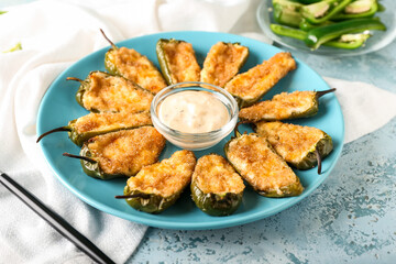 Delicious jalapeno poppers and sauce in plate on color background, closeup