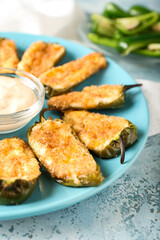 Delicious jalapeno poppers and sauce in plate on color background, closeup