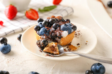 Plate with spoon and tasty berry tart on light background