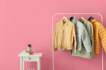 Rack with stylish jackets near pink wall in hallway