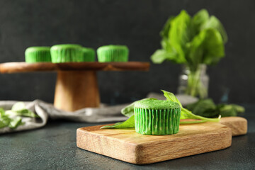 Wooden board with tasty spinach muffin on dark background