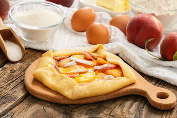 Board with raw peach galette on wooden table, closeup