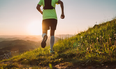 Active mountain trail runner dressed bright t-shirt with backpack running endurance marathon race by picturesque hills at sunset time back view photo. Sporty active people backlight concept image.