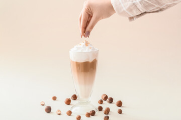 Woman adding nuts into glass of tasty latte on beige background