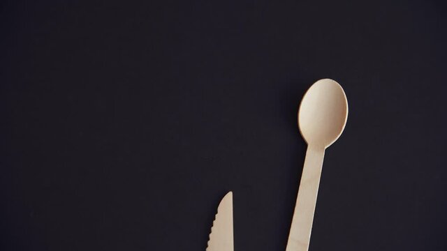 Person puts set of wooden disposable biodegradable cutlery (spoon, fork and knife) on black background. Top view. Environmental issues. Nature pollution reduction theme.