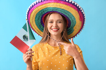 Happy young woman in sombrero hat and with flag of Mexico on color background