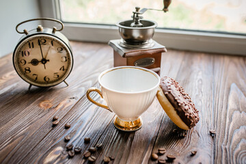 white kettle and cup on table. Breakfast by window. Chocolate donat next to scattered coffee beans.