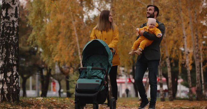 Young family walking with baby carriage at the autumn park with yellow trees