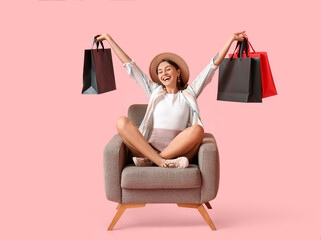 Happy young woman with shopping bags sitting in armchair on color background. Black Friday sale