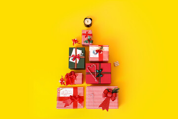 Christmas tree made of gift boxes and alarm clock on yellow background