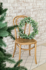 Wooden chair with mistletoe wreath near brick wall