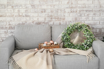 Sofa with Christmas balls and mistletoe wreath near brick wall