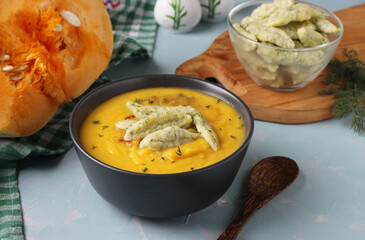 Pumpkin cream soup with cheese dumplings in dark bowl on light blue background, Horizontal format