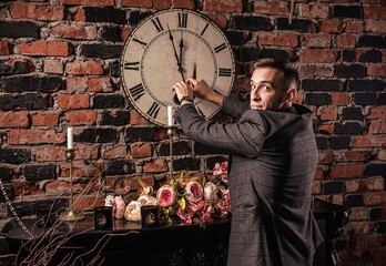 Fototapeta na wymiar a man in a formal suit and a Christmas hat with a microphone with a sparkler in his hand and a clock in the background