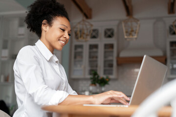 The blogger is working on a laptop. Workplace in the kitchen. A freelancer prints a message to clients on a social network. Student at home online learning. A woman surfing the internet.