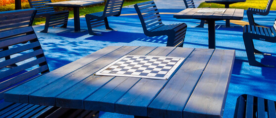 Selective focus on a blank chessboard on the table outdoors. Chess tables on a background of blue...