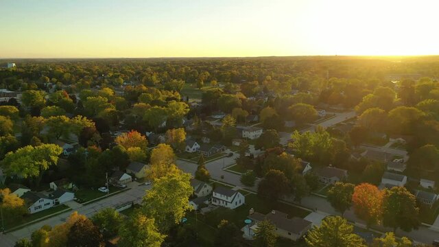 Sunset highlights autumn neighborhood scene with homes and colorful trees along the street, aerial drone shot