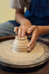Close-up of unrecognizable potter with wet dirty hand molding walls of clay pot on pottery wheel