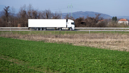 White truck driving on asphalt road in a rural landscape.