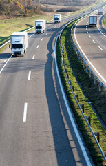 Small and large trucks drive on the highway. Highway transportation scene with Caravan or Convoy of White transportation trucks in line on a rural highway under a dramatic sky.
