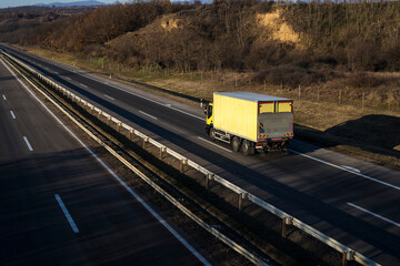 Yellow truck driving on asphalt road in a rural landscape.
