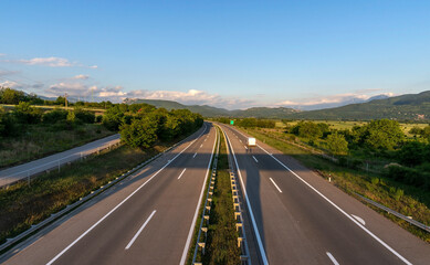 Obraz premium White truck in the countryside passing through green-blue nature on the highway.