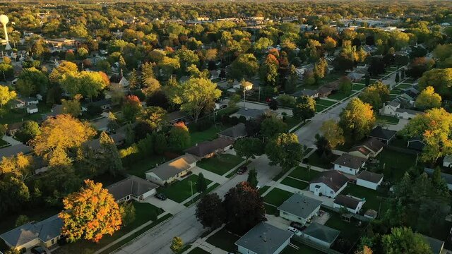 Sunset autumn neighborhood scene with homes and colorful trees, car driving down the street, aerial drone shot