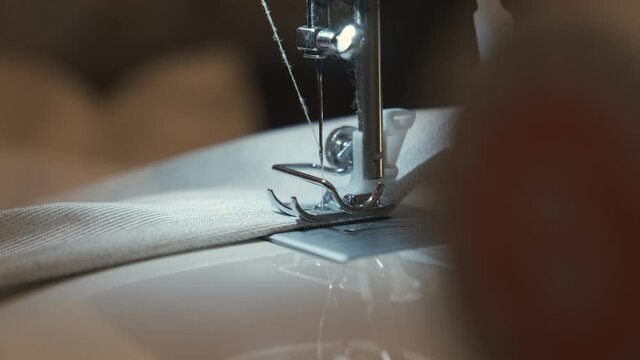Needle for sewing machine in motion. The close-up of the sewing machine needle quickly moves up and down. The seamstress sews gray fabric in the sewing workshop. The process of sewing the fabric.	