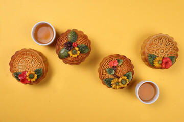 Colorful flower decorated moon cake Chinese mid autumn festival tea in small teacup on yellow background