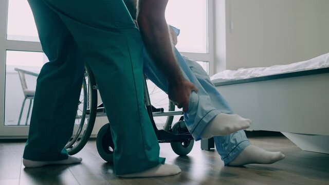Nurse transferring disabled man from wheelchair to bed in nursing home, care
