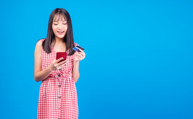 Financial payment online shopping and money transfer concept. Cheerful smile young woman holding smart phone and mockup credit card for internet banking while standing over isolated blue background.