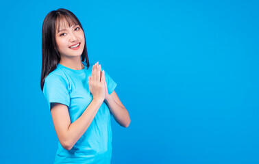 Lifestyle thai girl concept. Confident active young woman with black long hair wear casual holding own hands sign greeting Sawasdee or hello style Thailand while standing over isolated blue background