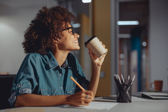 Smiling pretty woman in glasses drinking coffee while working in the modern office