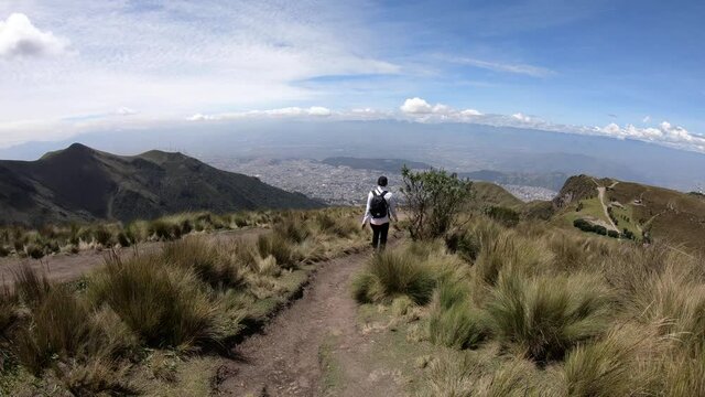 A woman is wearing a black backpack and a black cap while walking on a trail of Rucu Pichincha, on the moorlands of the Andes in Ecuador.