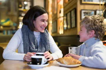 Happy woman enjoying communication with her preteen son while visiting cozy cafe..