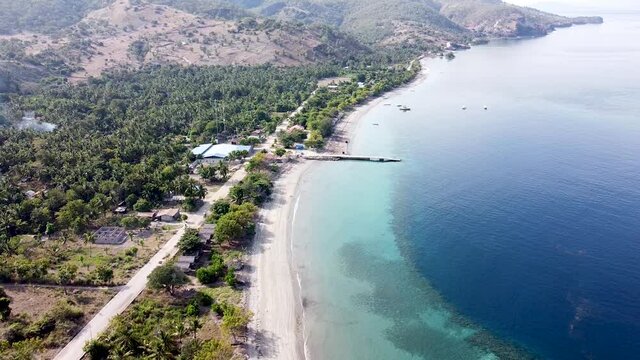 Aerial drone lowering towards a stunning rugged white sandy beach coastline and turquoise blue ocean on Atauro Island, Timor Leste