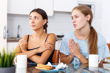 Portrait of unhappy girl friends discussion while drinking tea in home interior
