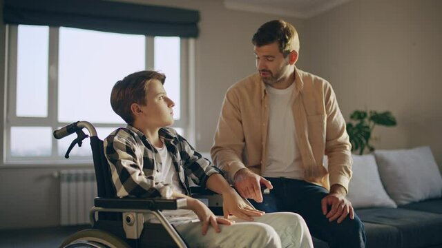 Loving dad talking to upset son in wheelchair, family support, recovery