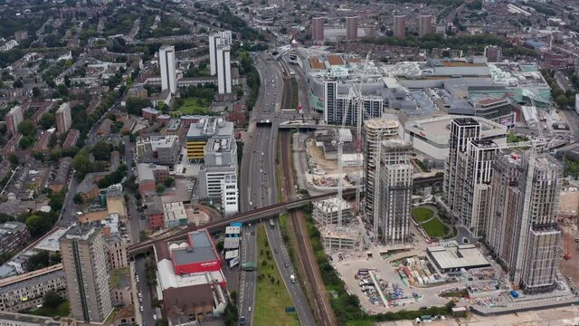 High angle view of multilane highway leading through urban neighbourhood. Static shot of construction site of new tall apartment buildings. London, UK