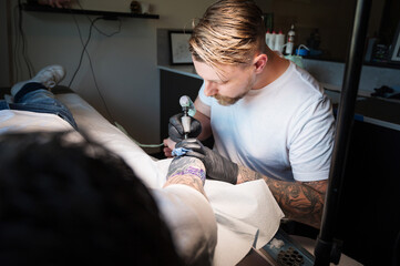 A tattoo artist works on a tattoo on the arm of a customer.