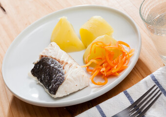 Steamed hake fillet served on white plate with boiled grated carrot and potatoes. Concept of diet food