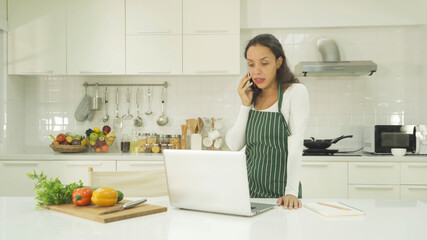 Relax happy latin young businesswoman. People talking on smartphone on social media internet and using a computer laptop notebook technology device in kitchen at home. Lifestyle